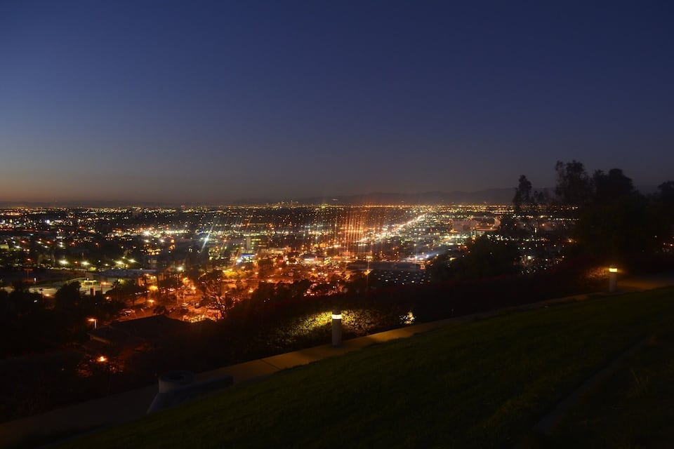 A cityscape at dusk with illuminated streets and distant mountains.