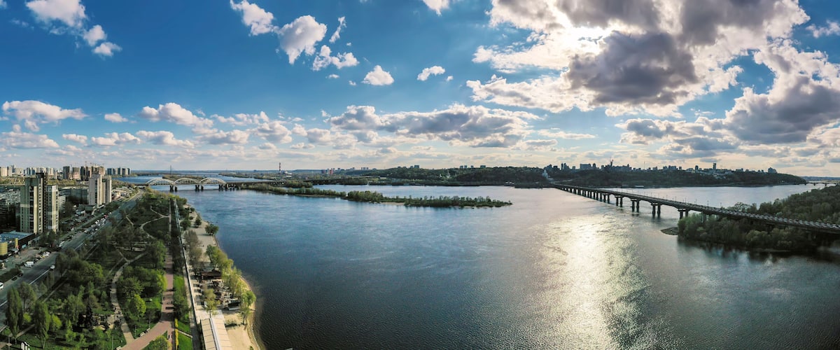 A river with a bridge, a city skyline, and a cloudy sky.