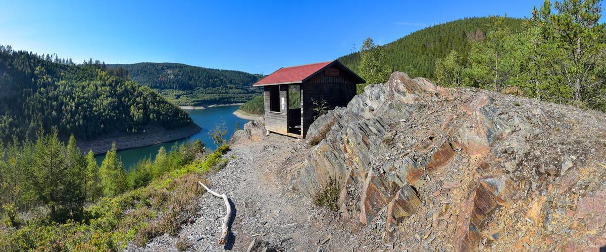 A wooden cabin on a rocky cliff overlooking a lake surrounded by dense forest.