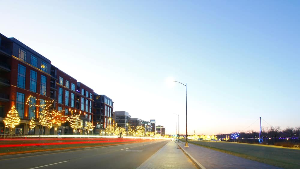 Eine Stadtstraße im Dämmerlicht mit beleuchteten Gebäuden und Straßenlaternen.