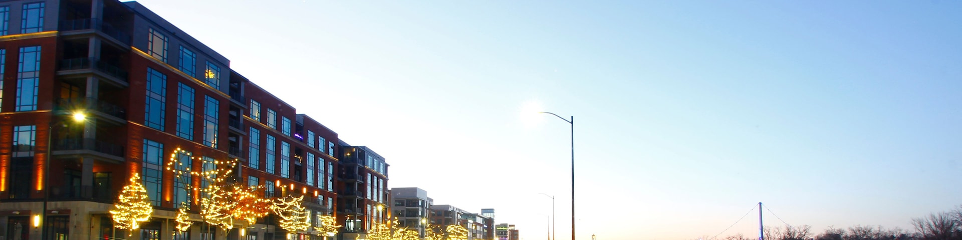 A city street at dusk with illuminated buildings and street lights.