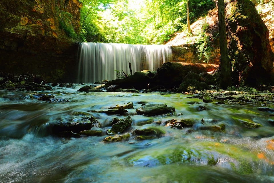 A waterfall in a forested area with a stream flowing below.