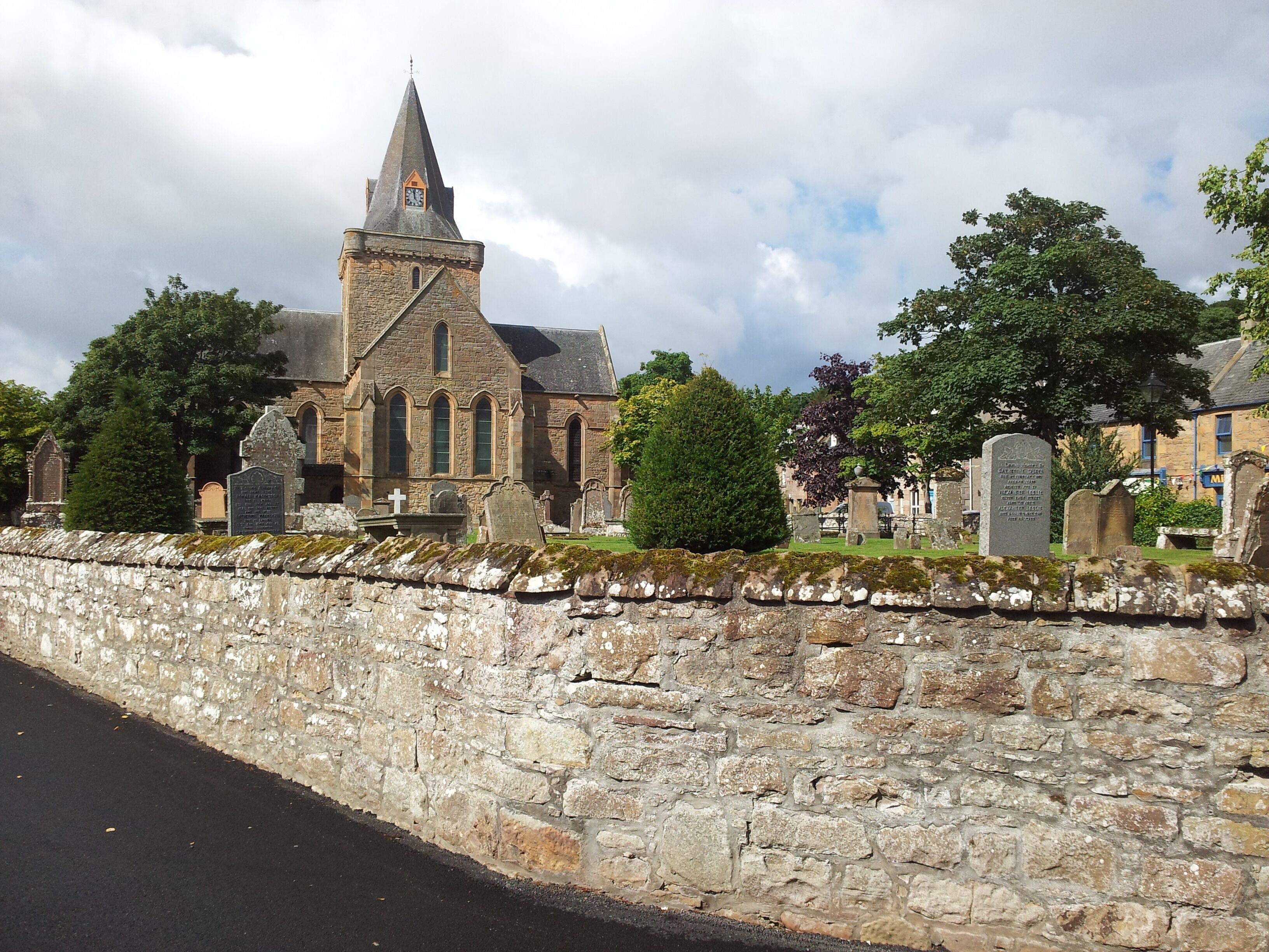 A historic church with a tall steeple, surrounded by stone walls and a cemetery.