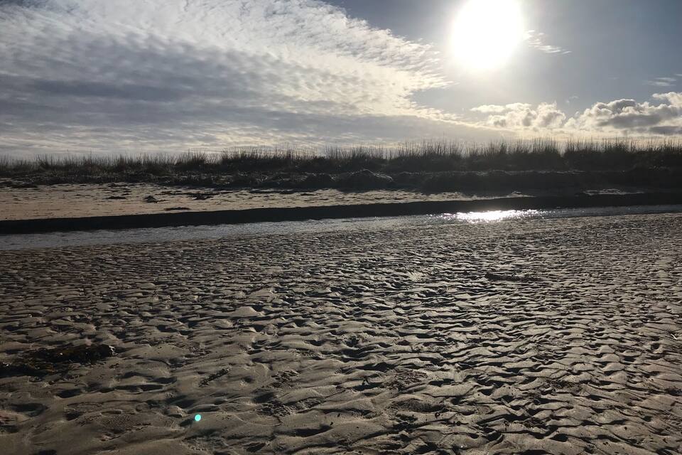 Platja amb petjades i un riu al fons.