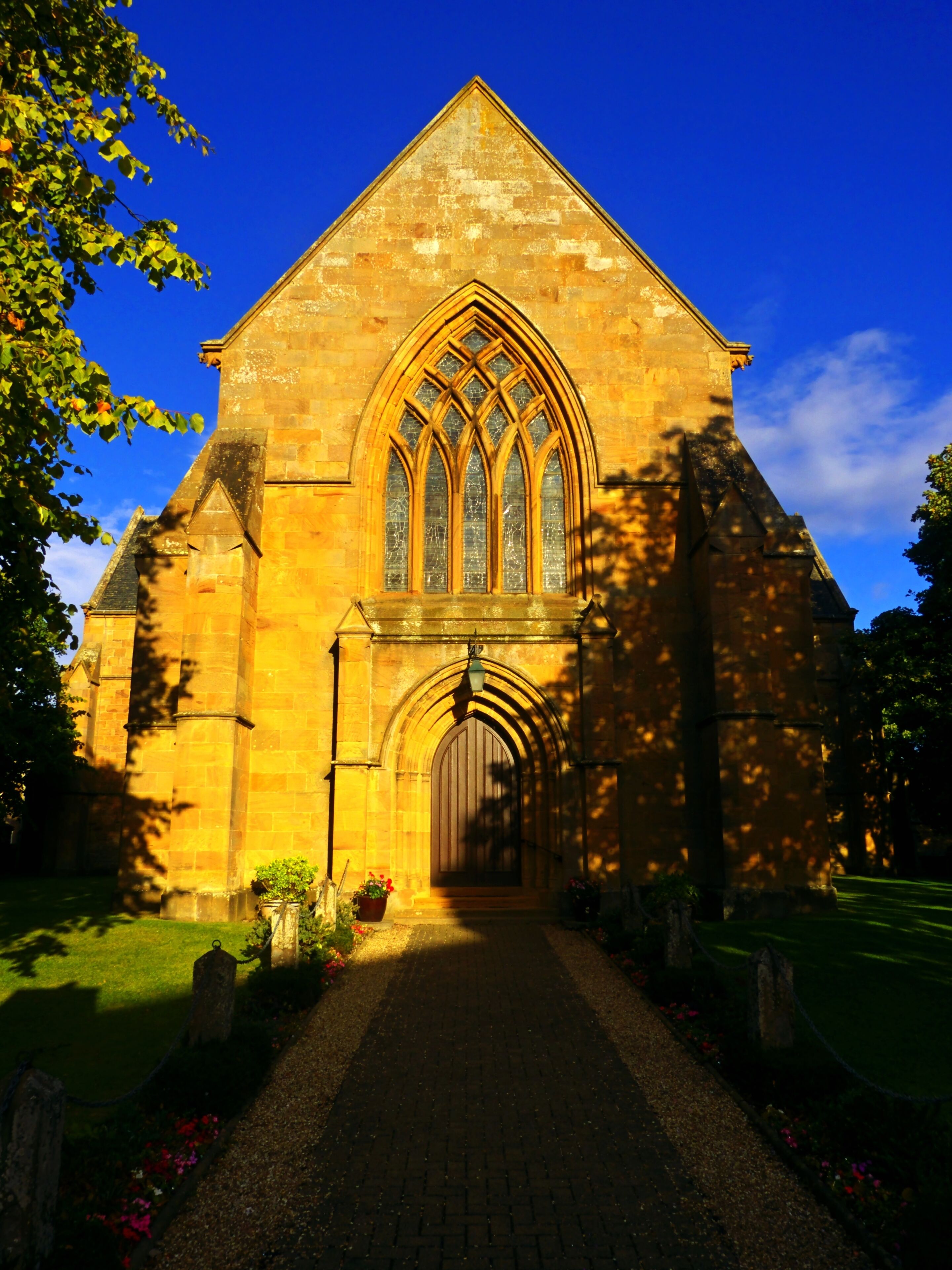 A stone church with a pointed arch window and a brick pathway leading to the entrance.