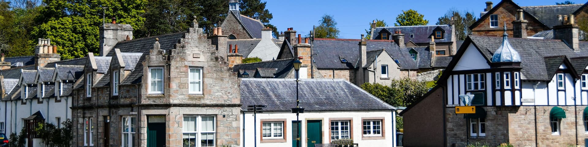 A quaint village street lined with historic stone buildings, a church spire, and a clear blue sky.