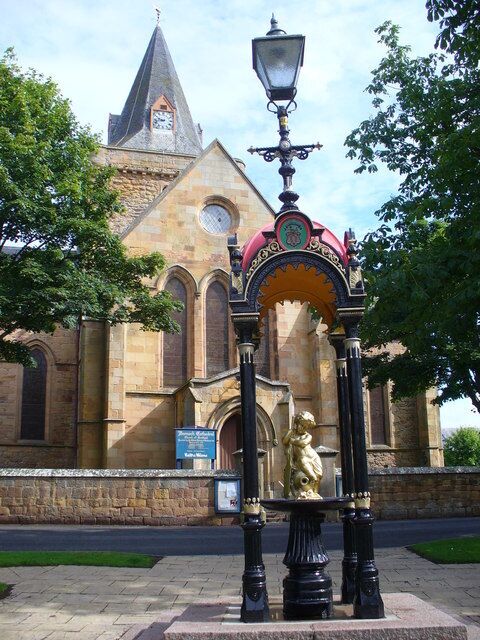A church with a clock tower, a street lamp, and a statue of a child.