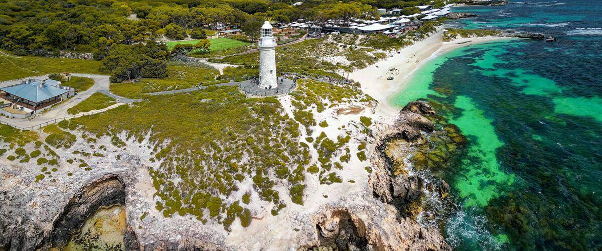 A coastal landscape with a lighthouse, beach, and rocky cliffs.