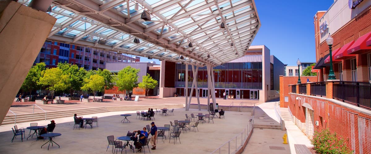 An outdoor plaza with a glass roof, surrounded by modern buildings and trees.