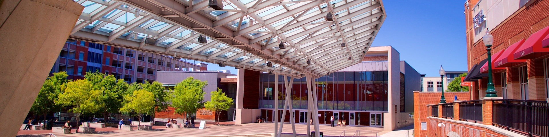 An outdoor plaza with a glass roof, surrounded by modern buildings and trees.