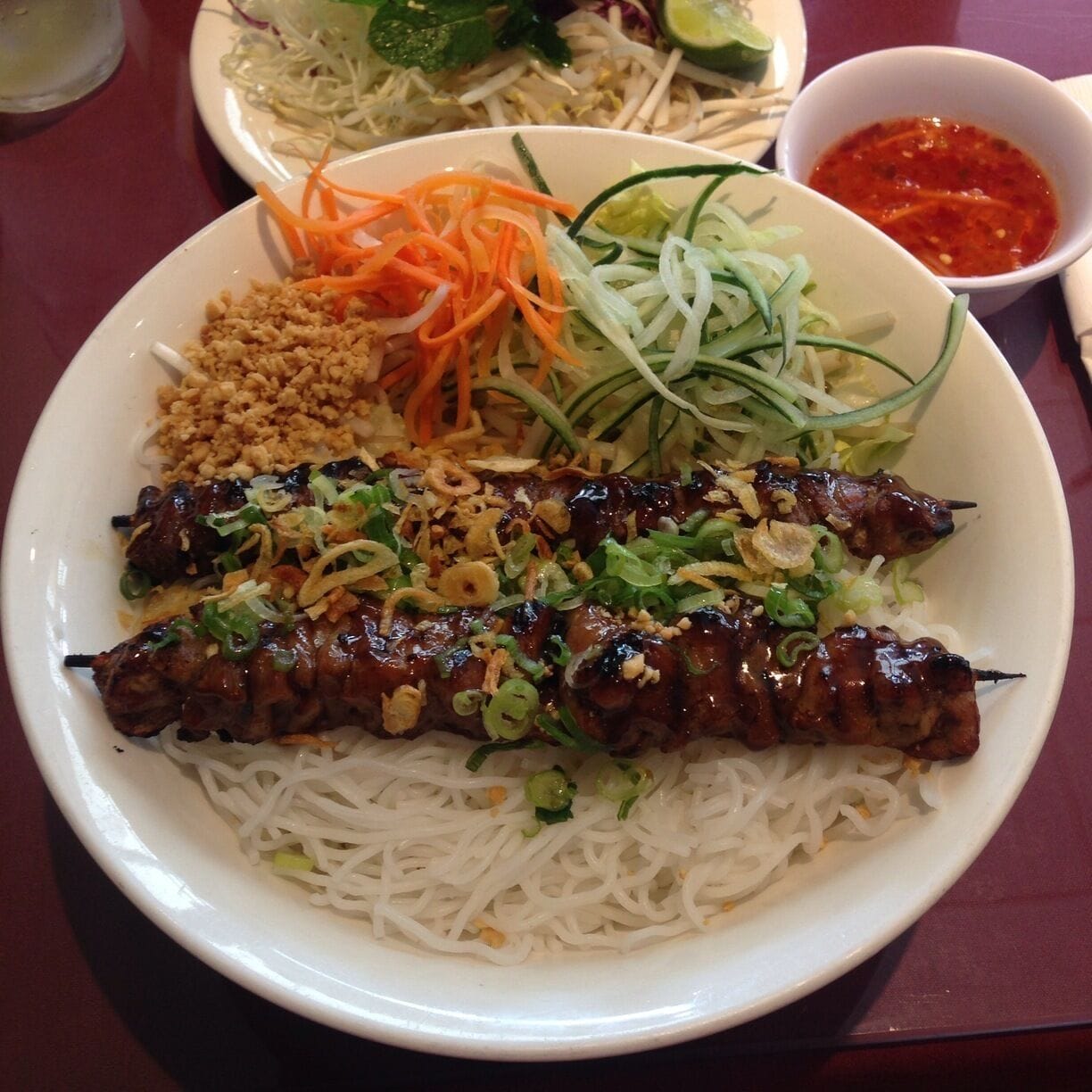 A plate of Vietnamese cuisine with grilled meat, noodles, and fresh vegetables.