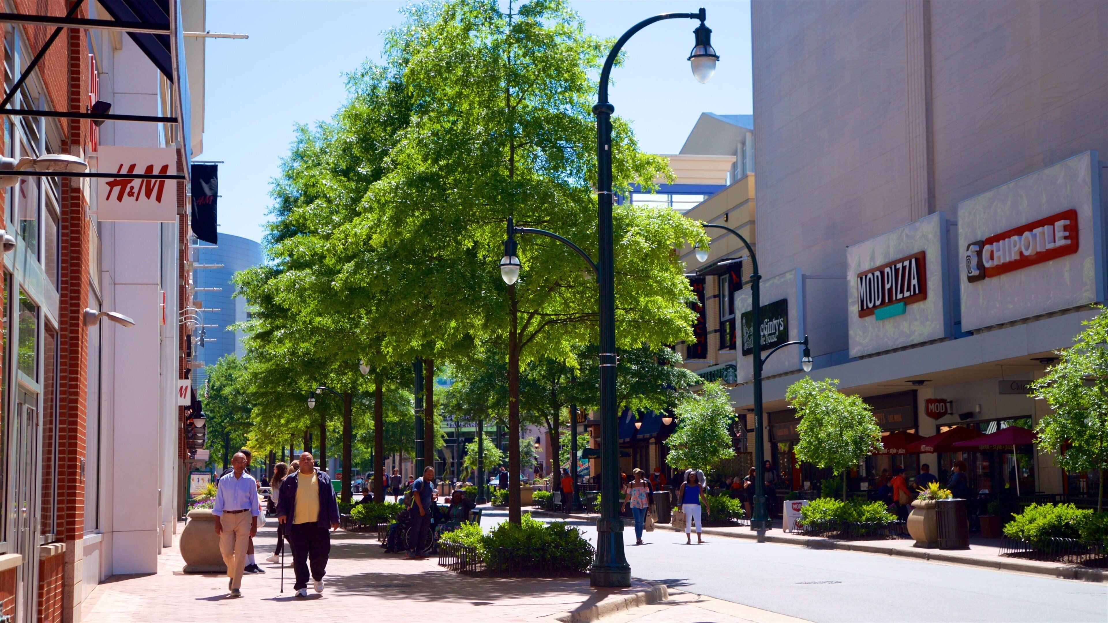 A city street lined with trees, storefronts, and pedestrians.