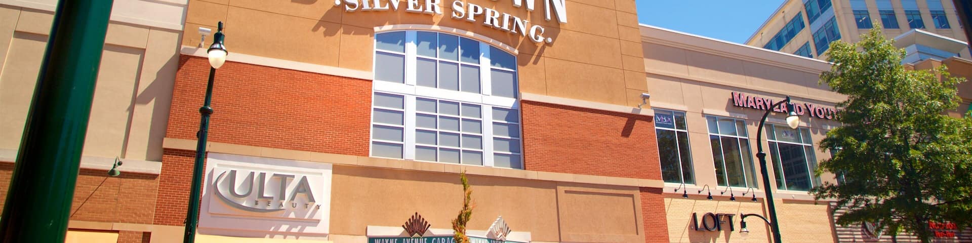 A downtown Silver Spring building with a clock, storefronts, and a parking sign.