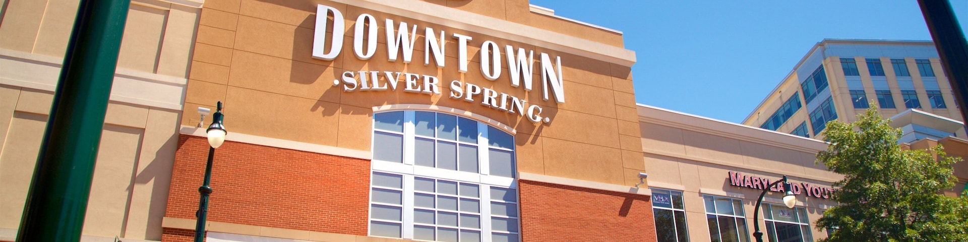 Un edificio en el centro de Silver Spring, con un reloj, locales comerciales y un letrero de estacionamiento.