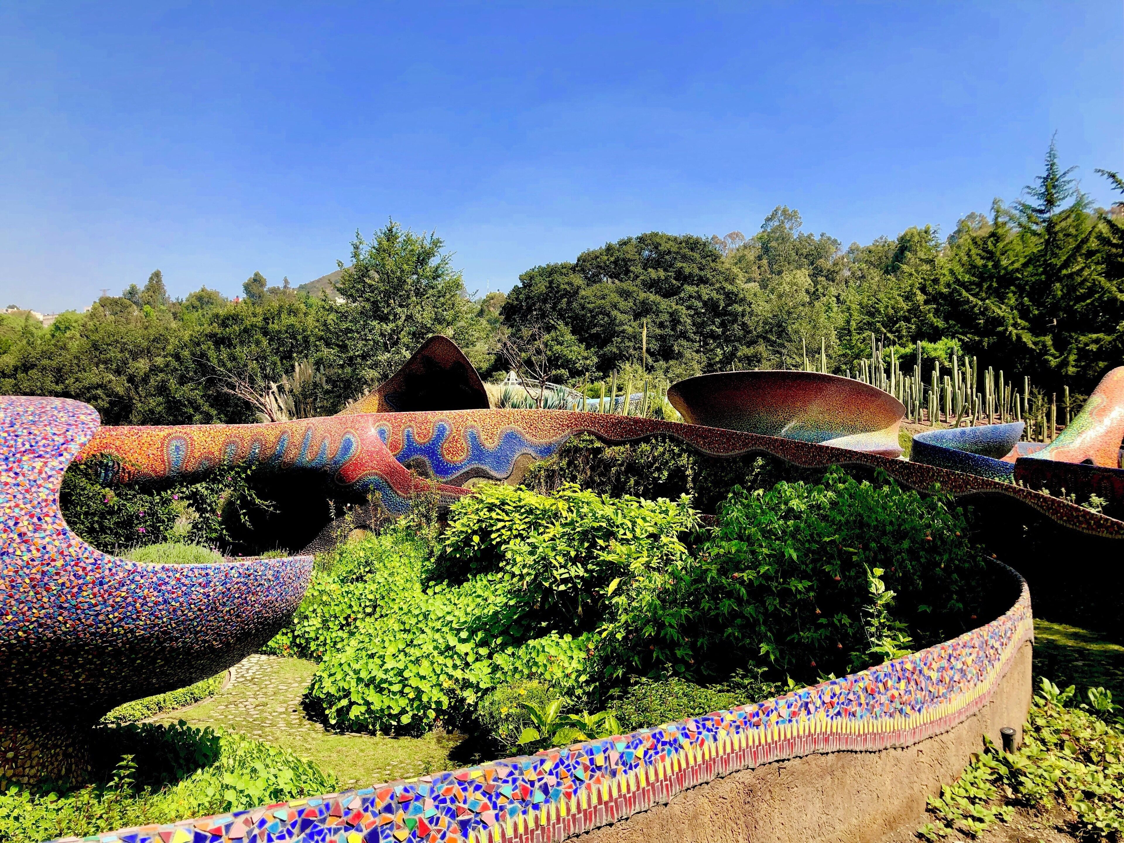 Un jardín con estructuras de mosaicos y abundante vegetación.