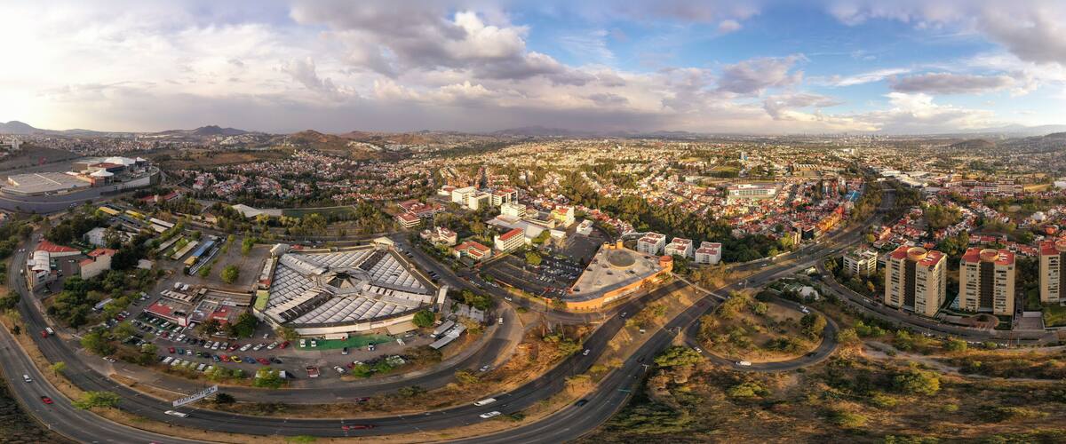 A panoramic view of a city with a mix of residential and commercial buildings, a large roundabout, and surrounding hills.
