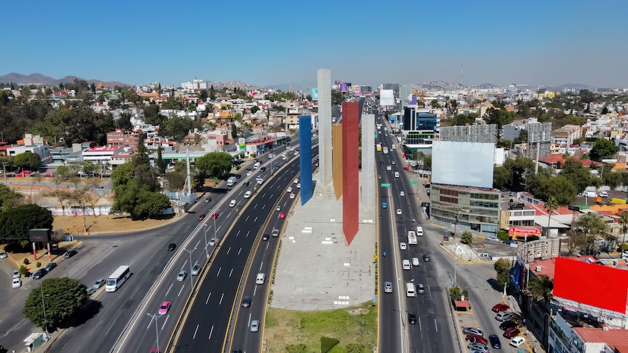 Paisagem urbana com uma rodovia em destaque, edifícios e montanhas ao longe.