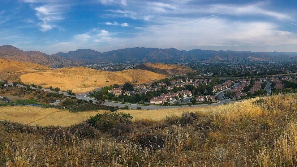 A valley with rolling hills, a town, and distant mountains under a partly cloudy sky.