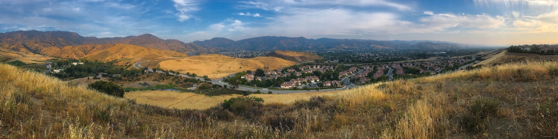 A valley with rolling hills, a town, and distant mountains under a partly cloudy sky.