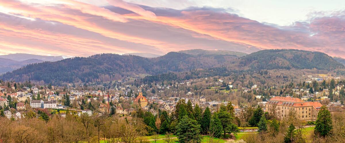 A town nestled in a valley with mountains in the background and a colorful sunset sky.
