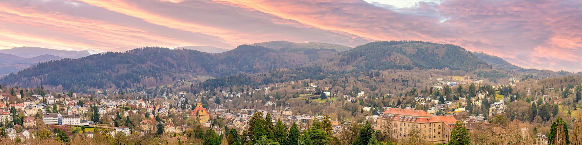 A town nestled in a valley with mountains in the background and a colorful sunset sky.