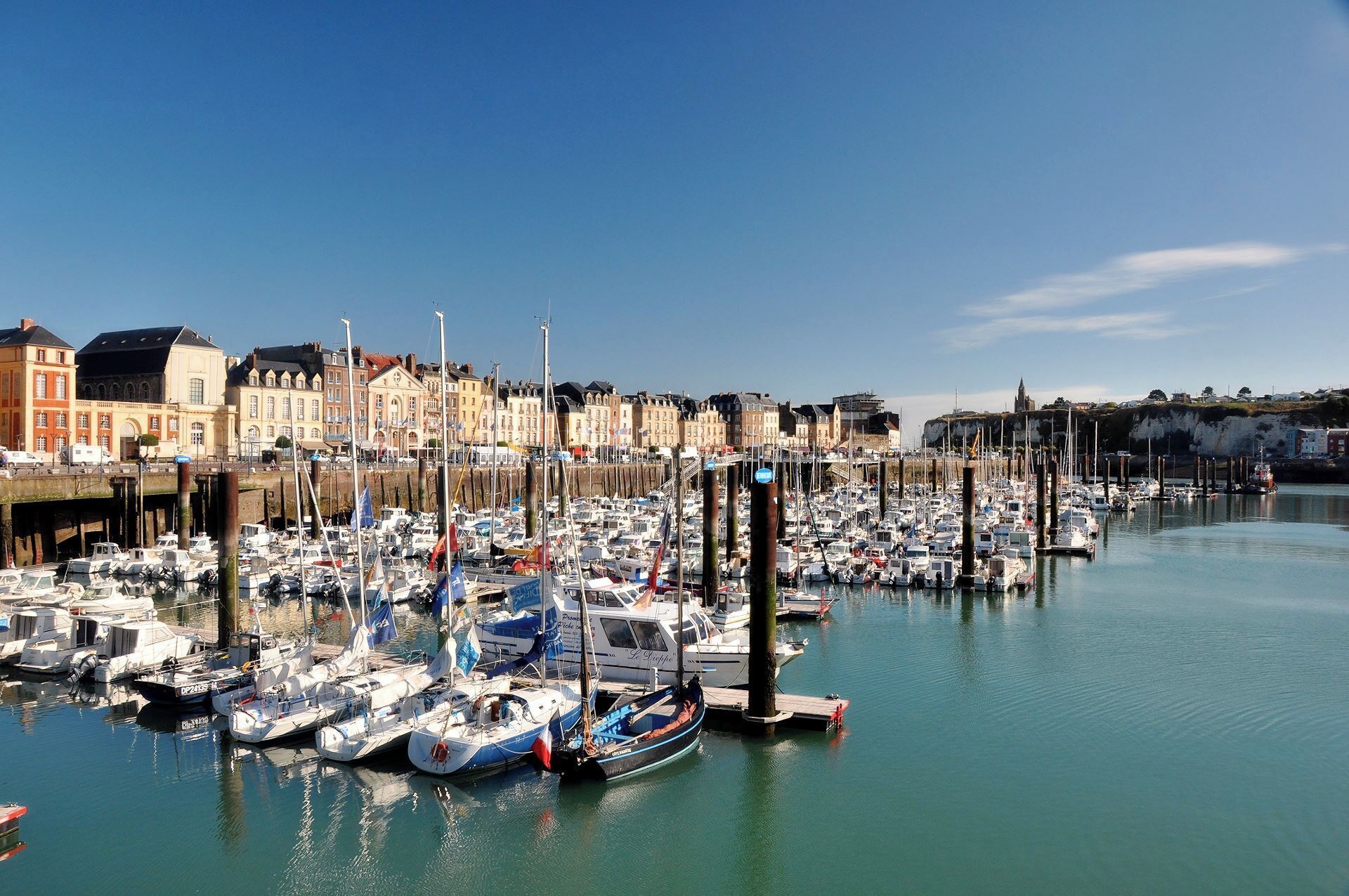 A marina with numerous boats docked, surrounded by historic buildings and a clear blue sky.