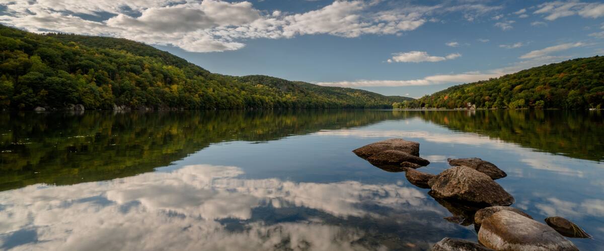 beautiful mountain lake in New England with a rock jetty and reflections of forest and sky