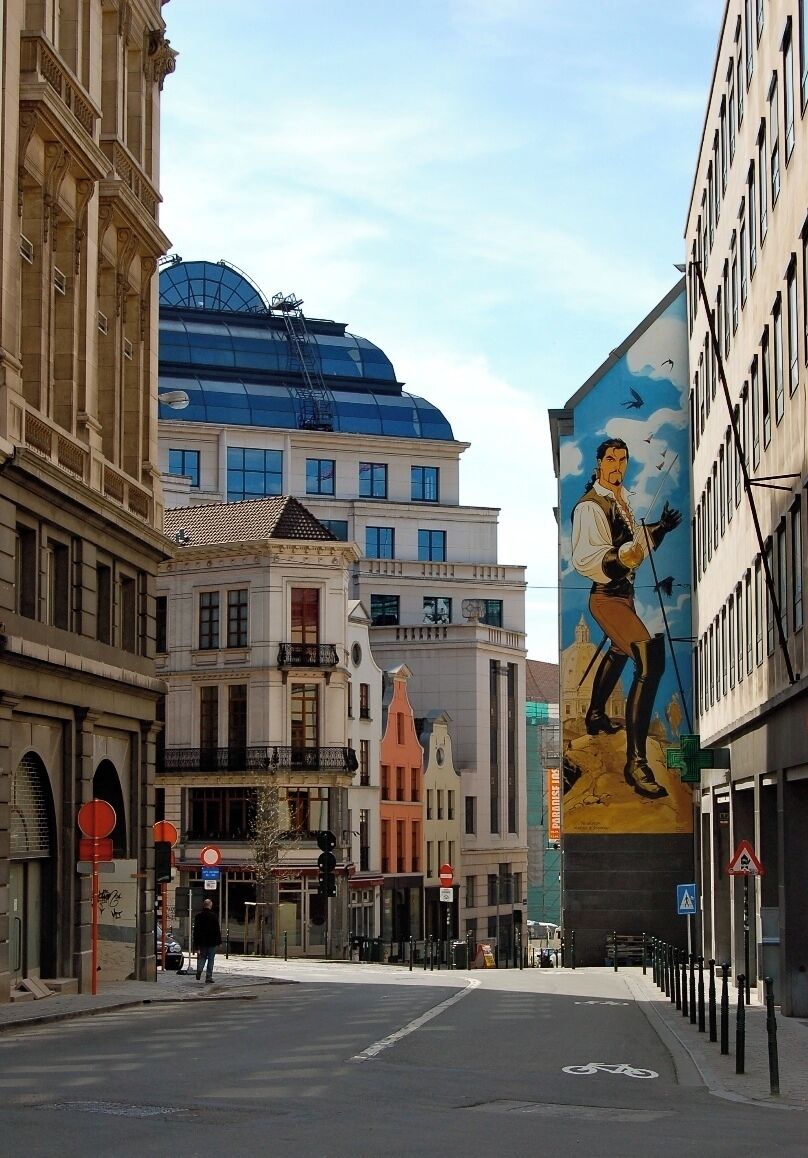 Ruas com edifícios históricos, um mural grande e uma estrutura de vidro moderna.