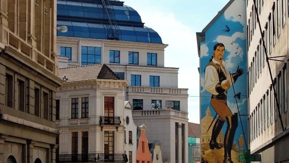 A street with historic buildings, a large mural, and a modern glass structure.