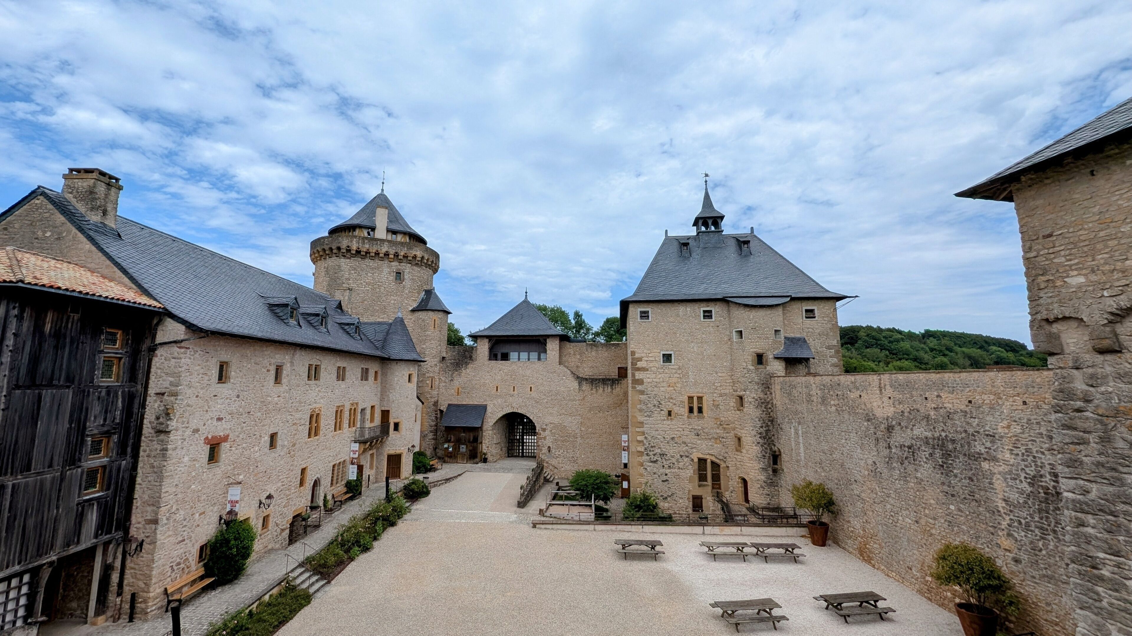 A historic stone castle with a courtyard, wooden buildings, and a tower.