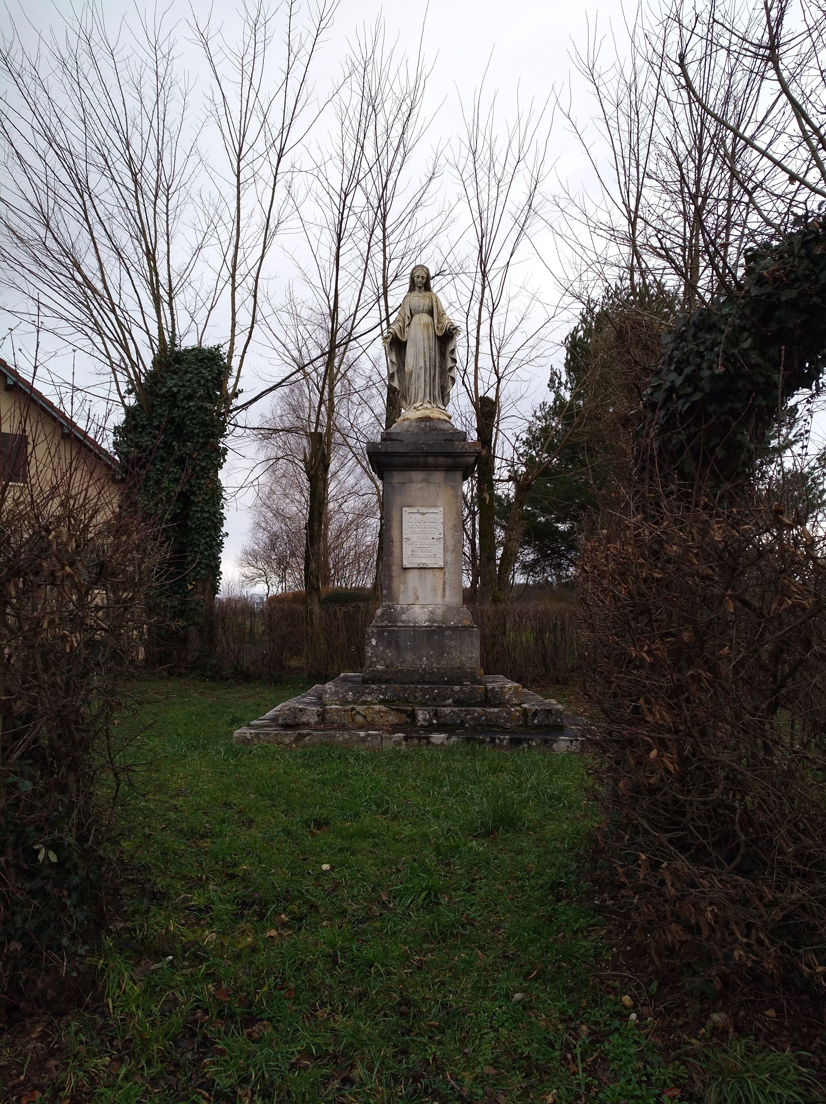 A statue in a grassy area surrounded by trees and bushes.