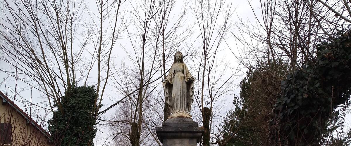 A statue in a grassy area surrounded by trees and bushes.