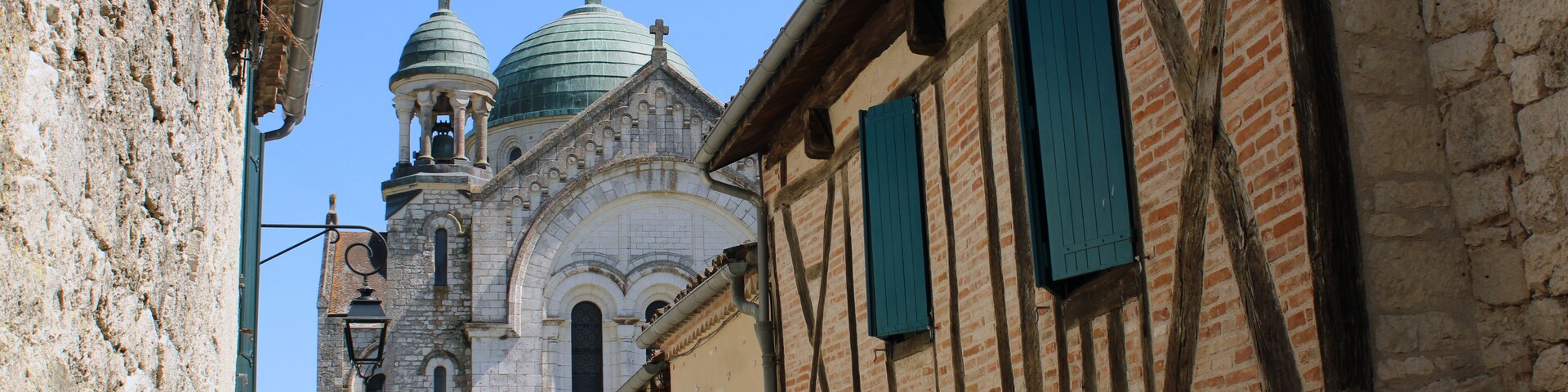 Une rue étroite bordée de bâtiments historiques, une église coiffée de coupoles et un ciel d’un bleu limpide.