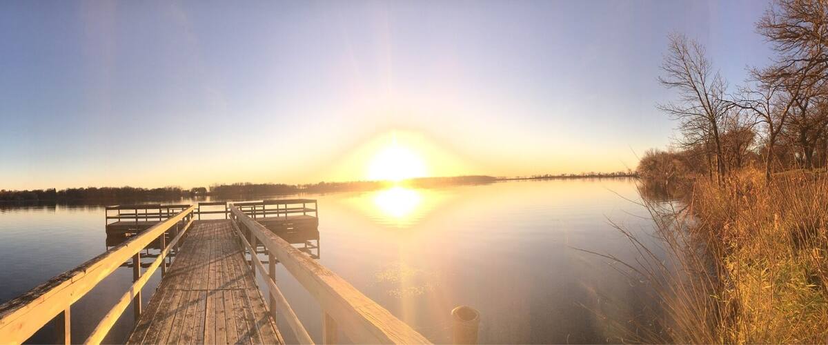 A wooden pier extending into a calm lake at sunrise with a clear sky.