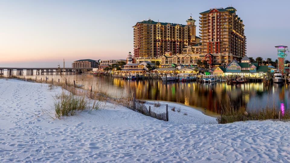 A snowy beach with a pier, boats, and buildings reflecting on the water.