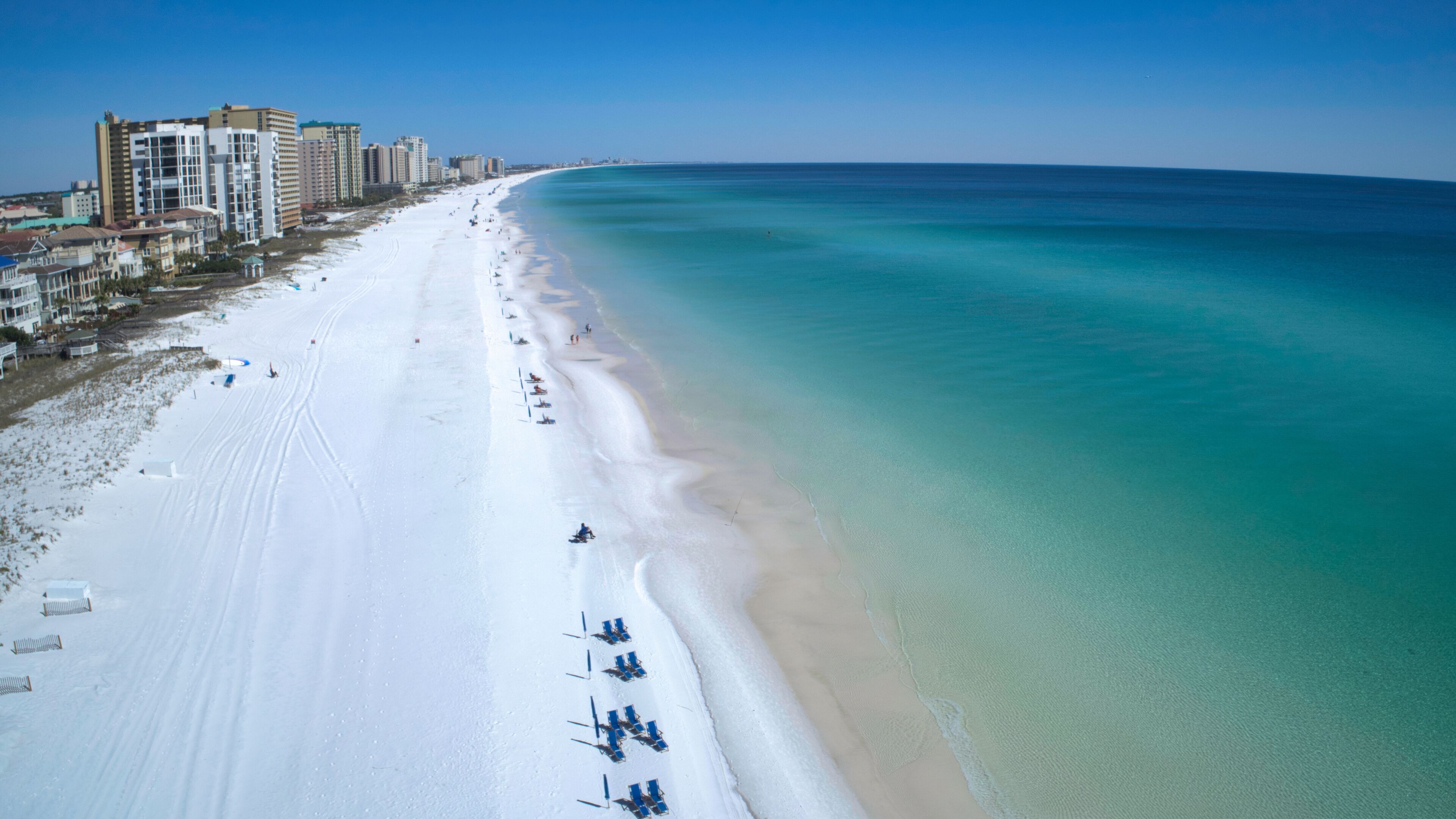 A beach with white sand, clear turquoise water, and a row of beach chairs along the shoreline.