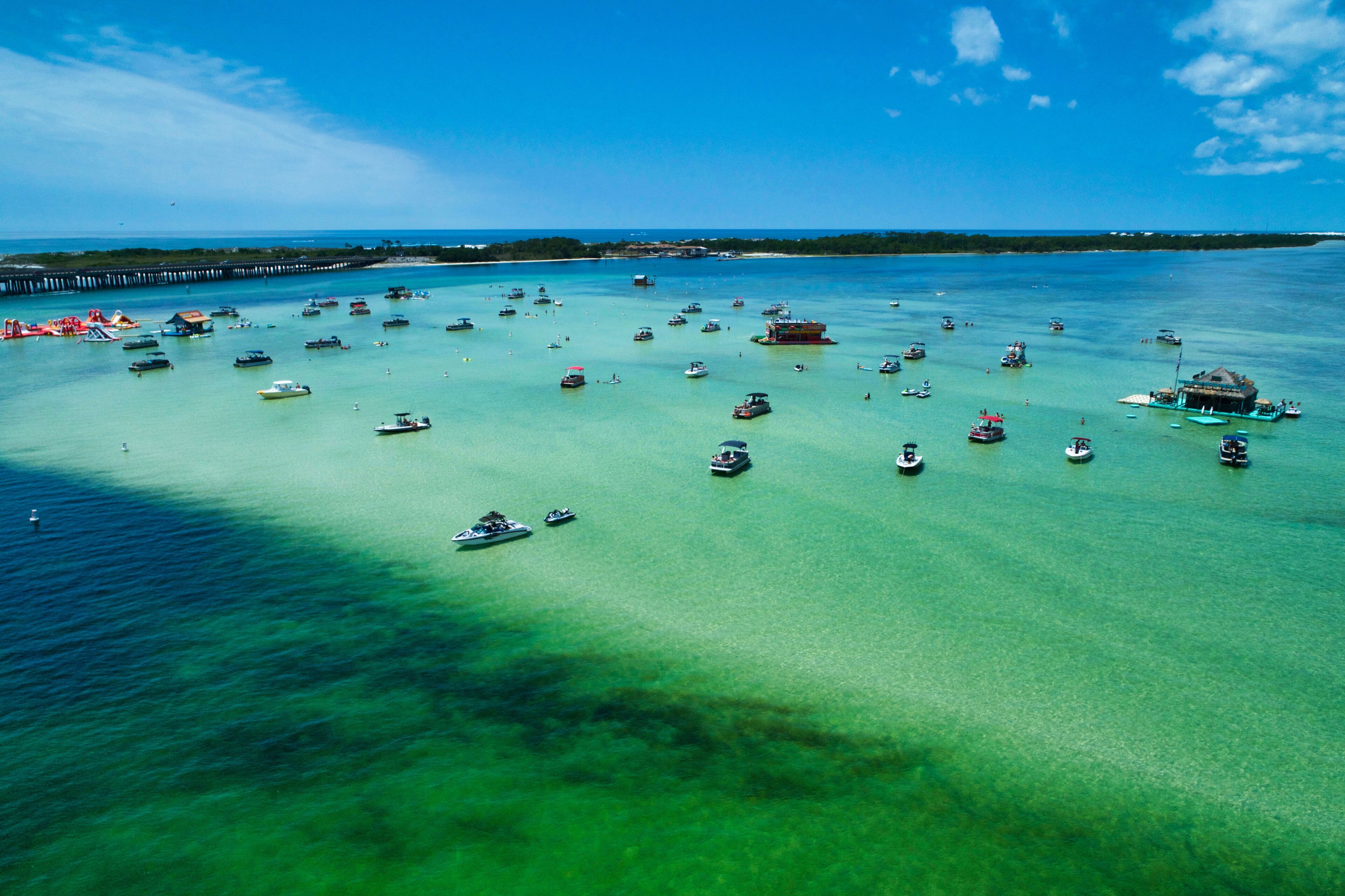 A tropical island with clear turquoise waters, numerous boats, and a pier.