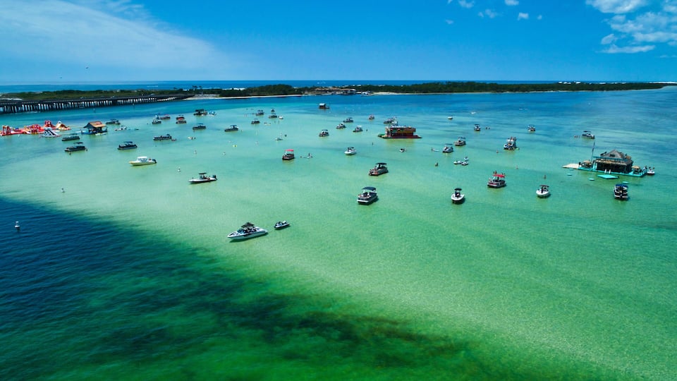 A tropical island with clear turquoise waters, numerous boats, and a pier.