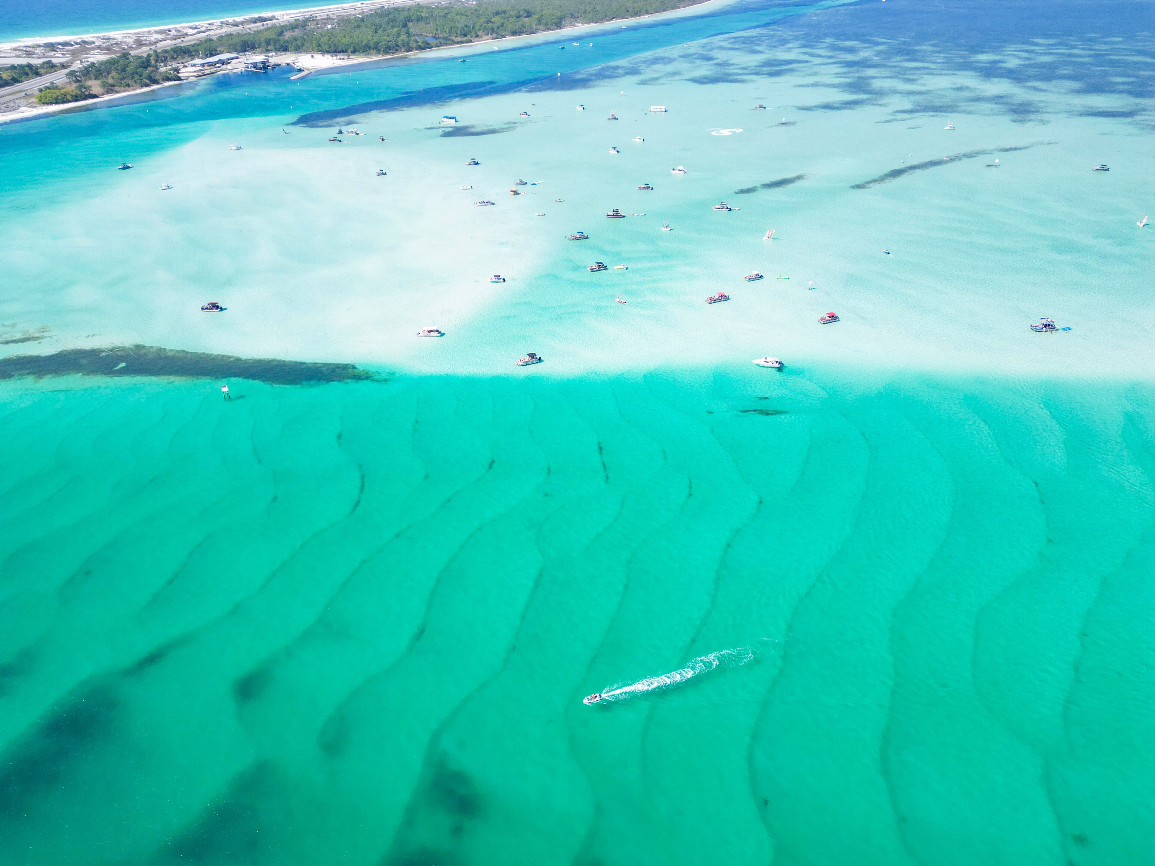 An aerial view of a turquoise sea with shallow waters and a boat in the foreground.