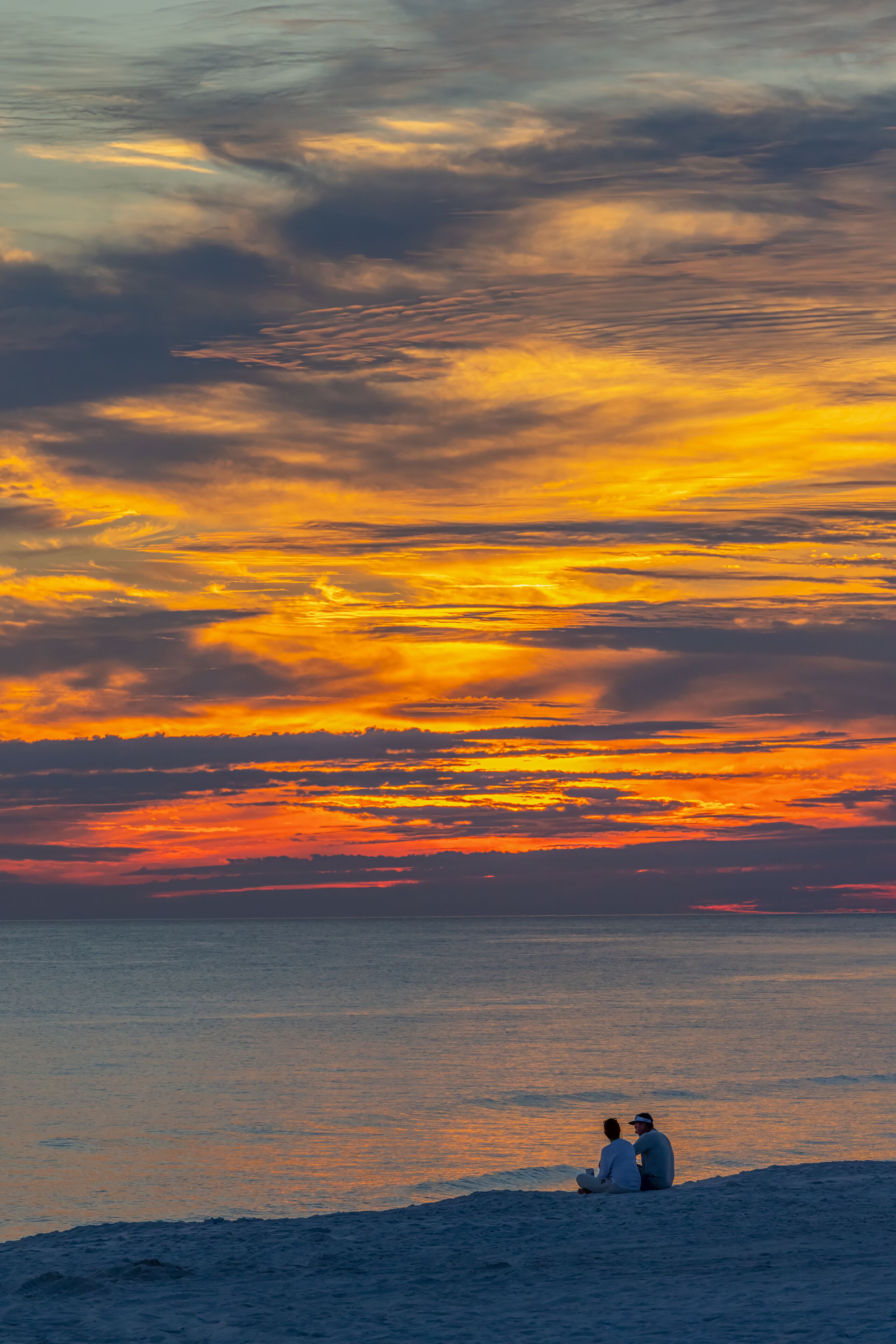 A sunset over a body of water with two people sitting on the shore.