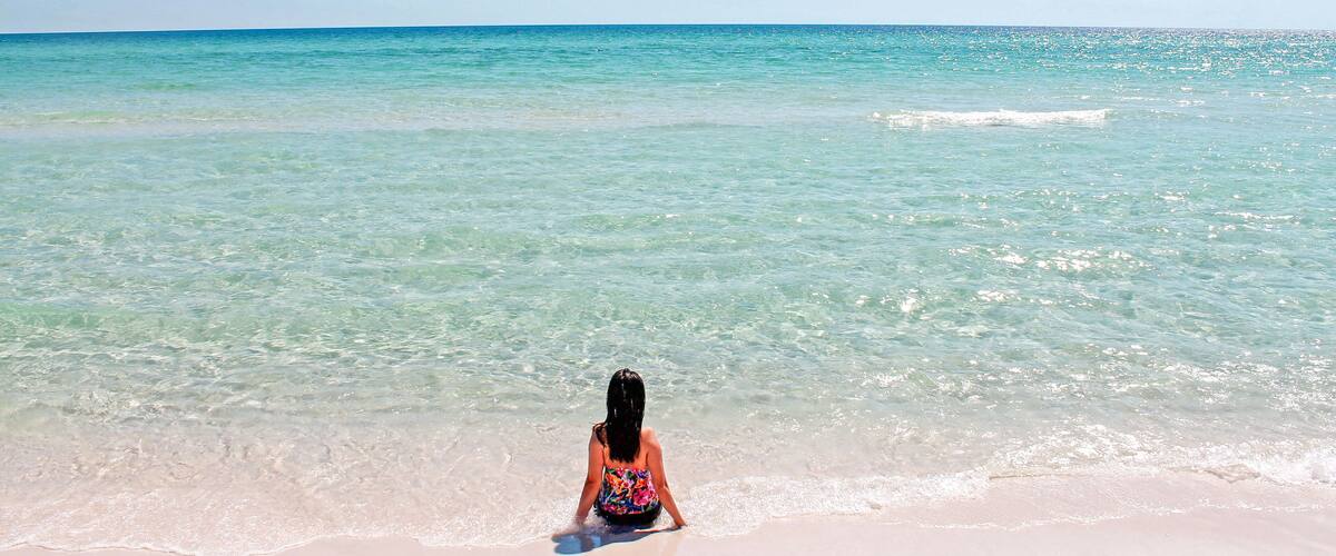 A person sitting on a sandy beach facing the ocean.