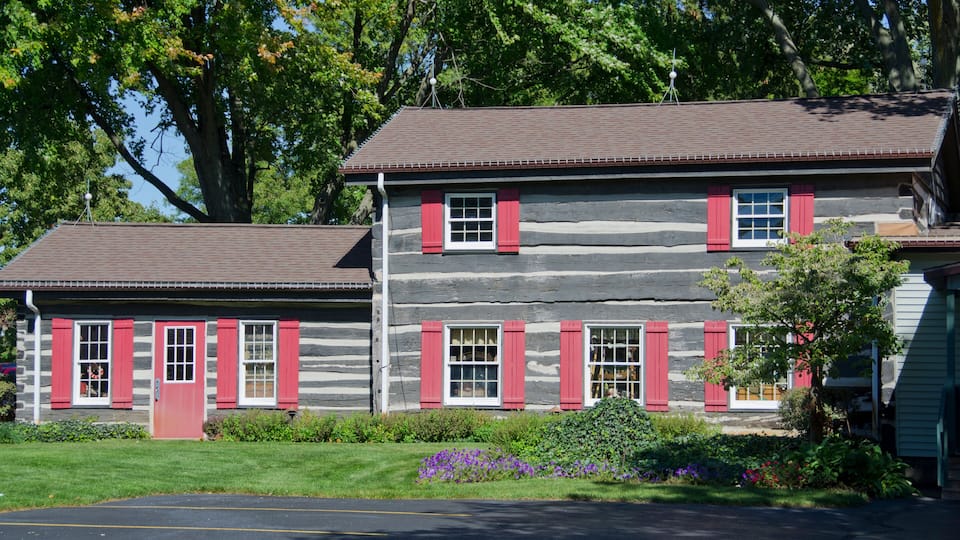 A log cabin with red shutters and a small porch.