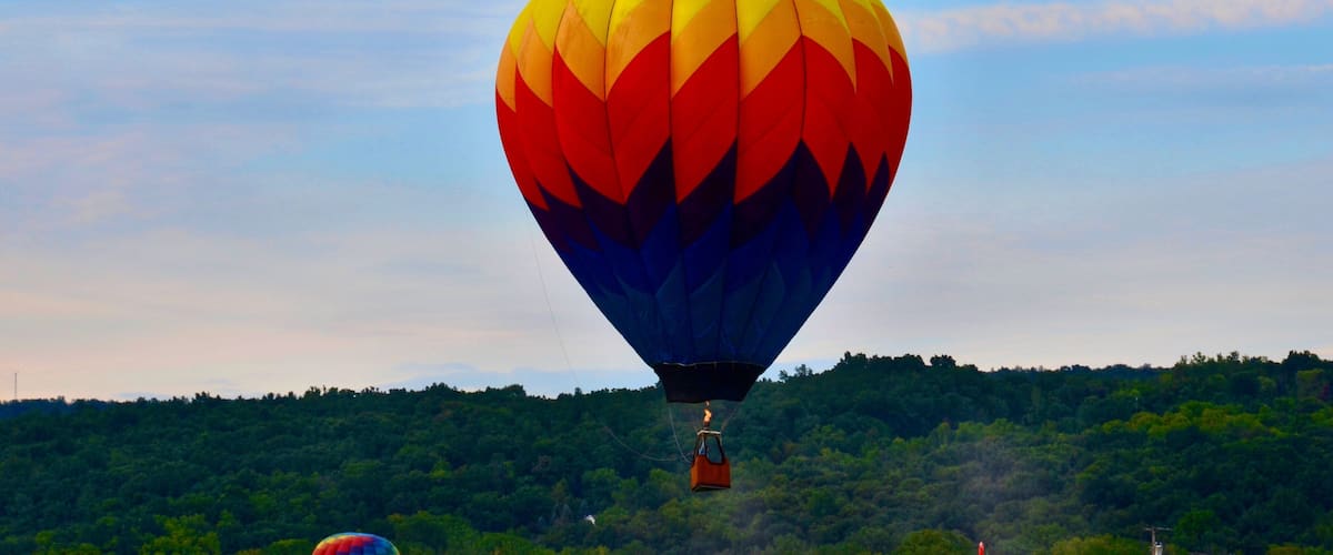 A hot air balloon with a rainbow pattern flying over a forested area.