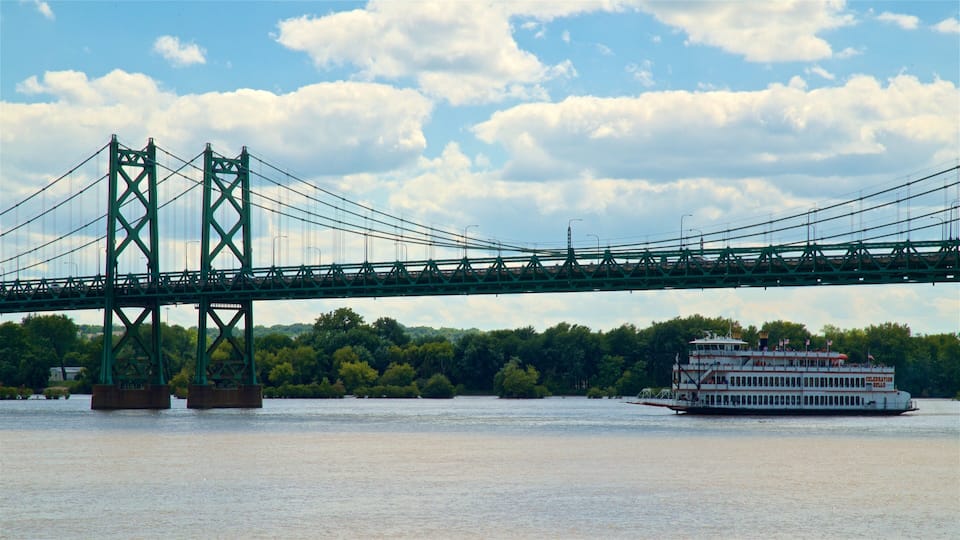 A large green bridge spanning a river with a white riverboat docked on the right.