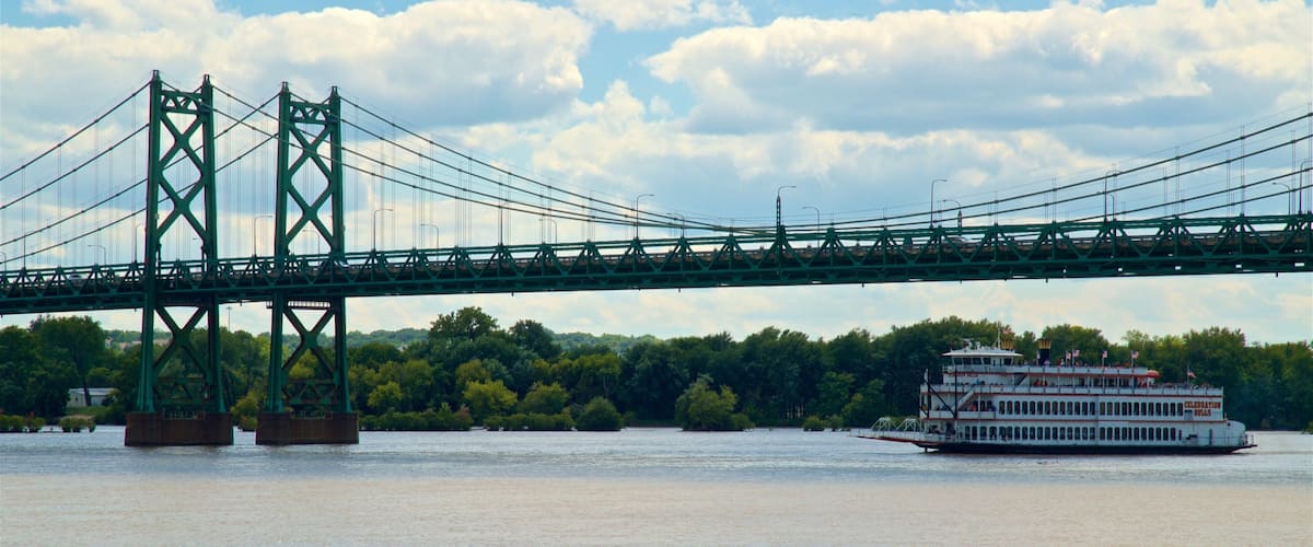 A large green bridge spanning a river with a white riverboat docked on the right.