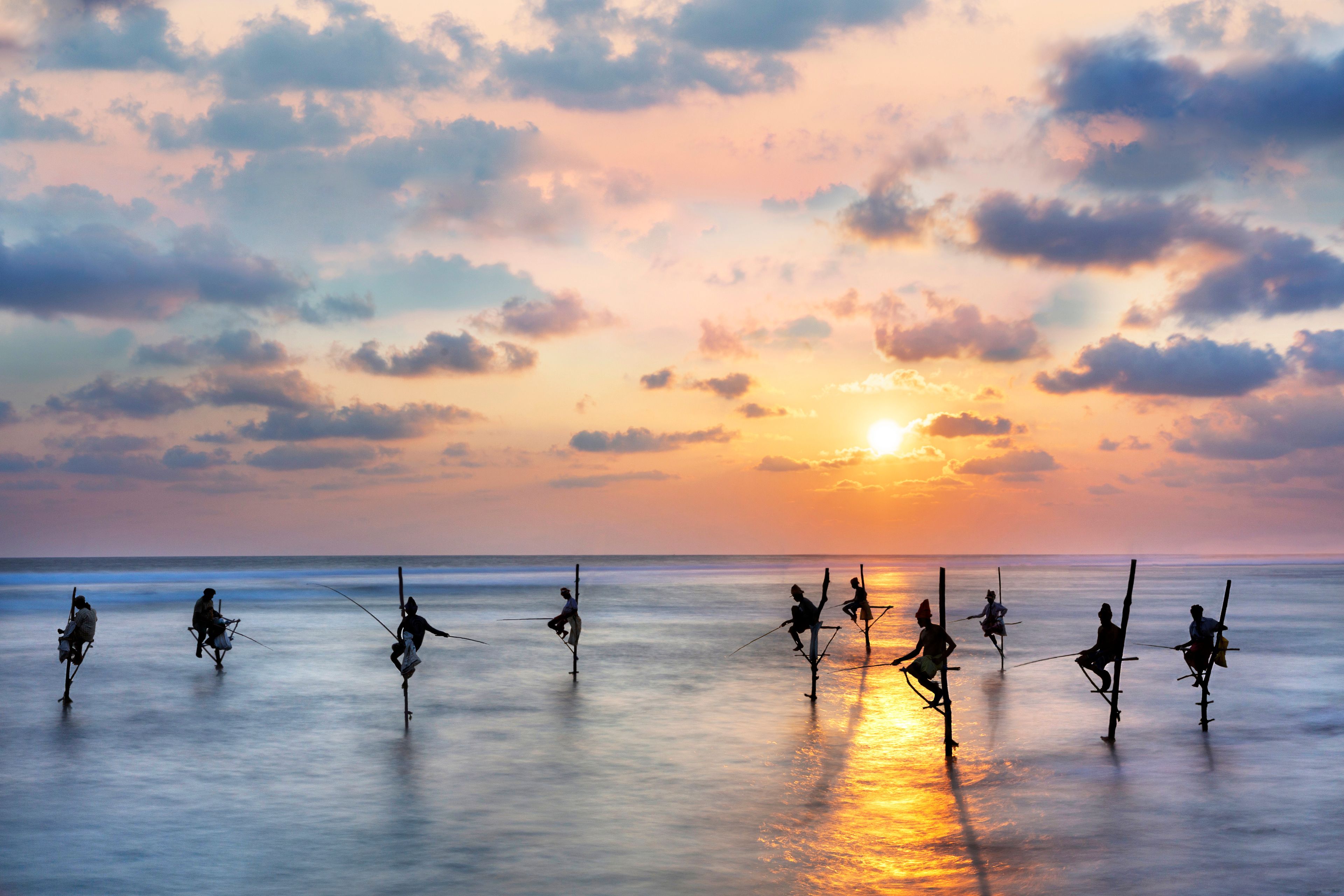 Un atardecer sobre un mar tranquilo con gente pescando.