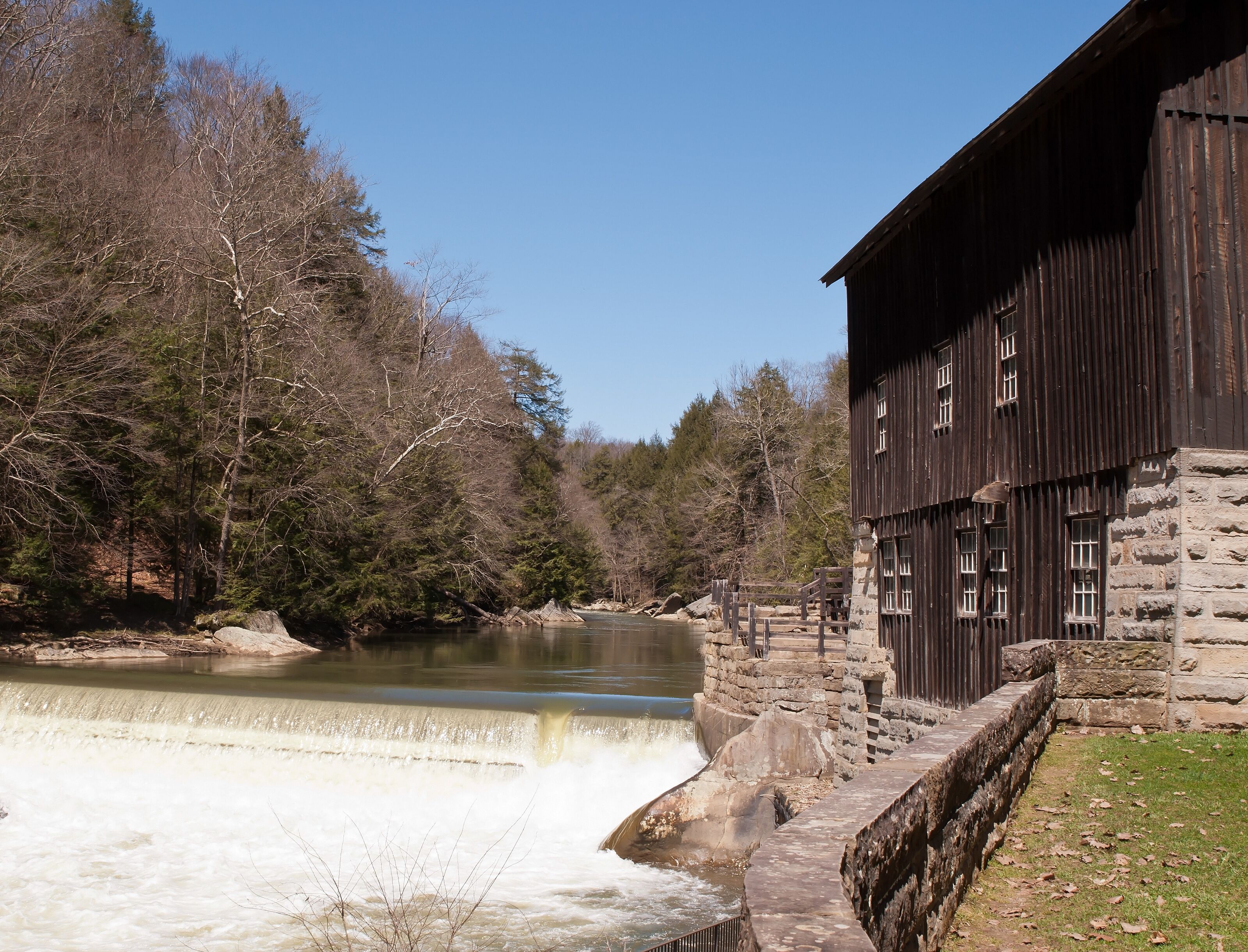 A river with a dam, a wooden building, and a forested area.