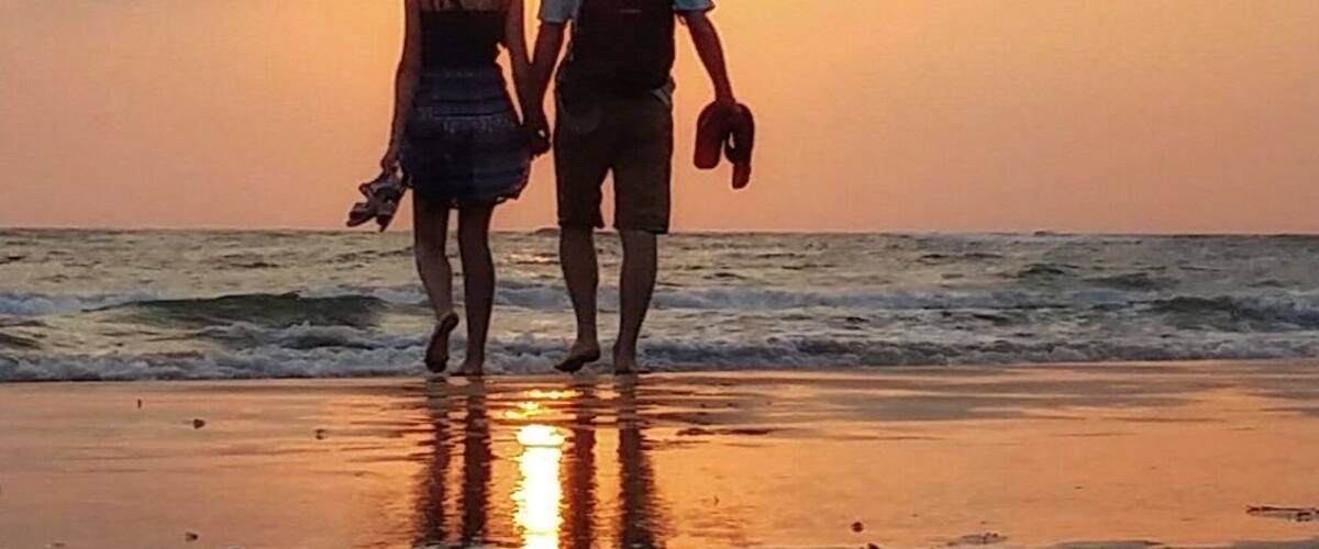 A couple walking on a beach at sunset with the sun reflecting on the water.