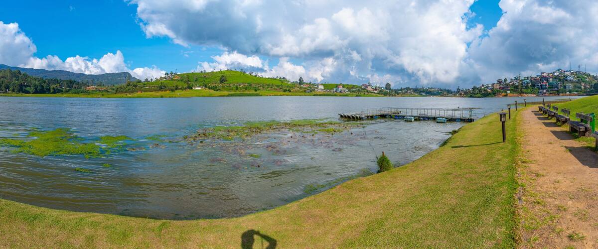 A lake with a dock, grassy banks, and a distant town with hills.