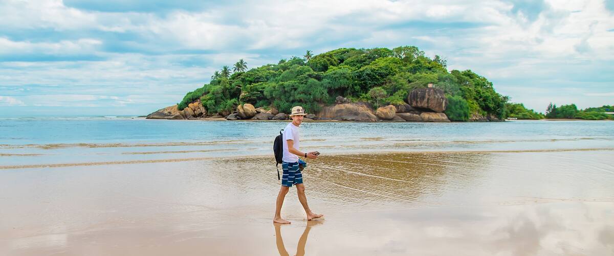 A person walking on a beach with a small island in the background.